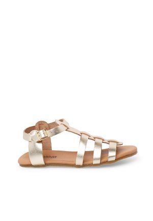 Flat sandal with gold metallic straps and a buckle closure on a tan sole, side view on a white background.