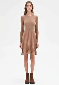 Geripptes Midikleid in Hellbraun, mit langen Ärmeln, tailliertem Oberteil und ausgestelltem Rock. Kombiniert mit dunkelbraunen Stiefeletten.