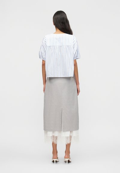 Γυναίκα που φοράει μπλούζα με μπλε ρίγες και κοντά μανίκια, γκρι μίντι φούστα με άνοιγμα πίσω, λευκή δαντελωτή εσώφουστα και λευκά mules με τακούνι, ενώ είναι γυρισμένη από την πλάτη.