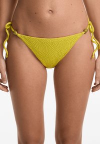 Gelber Bikiniunterteil aus strukturiertem Stoff, mit seitlichen Bindebändern und runden Hardware-Details. Hat einen niedrigen Schnitt und ein gewelltes Design.