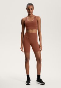 Rjava atletska kratka majica in ujemajoče kolesarske hlače, narejene iz raztegljivega materiala, z visokim pasom in minimalnimi šivi. Črne atletske čevlje.