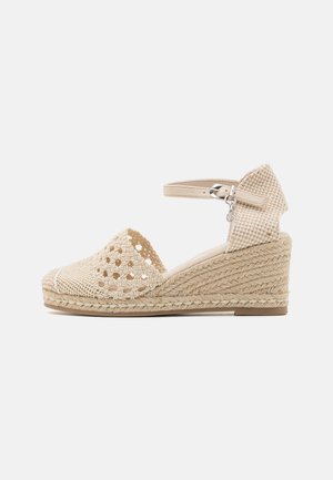 Sandalia de cuña de esparto trenzada en beige, con punta abierta, correa al tobillo y tacón envuelto en yute. Presenta un diseño perforado y acentos de tela texturizada.