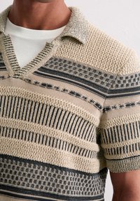 Sweter polo w kolorze beżowym i ciemnoniebieskim, z teksturowanymi wzorami, w paski oraz płytkim kołnierzykiem w kształcie V. Krótkie rękawy.