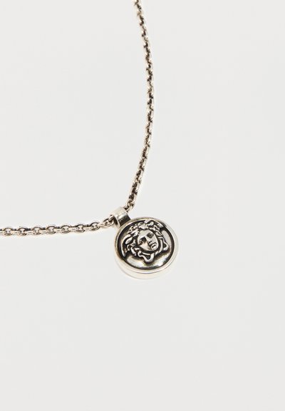 Ασημένιο κολιέ με αλυσίδα και στρογγυλό μενταγιόν που απεικονίζει ανάγλυφη κεφαλή Μέδουσας σε απλό φόντο.