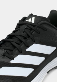 Black athletic shoe featuring a mesh upper, black laces, and three prominent white stripes on the side. Durable rubber sole.