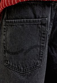 Mustade teksade tagatasku makropilt, kus on nähtavad õmblused ja osa punase-valge triibulise topi osast.