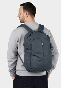 Zaino grigio con spallacci imbottiti, scomparti con zip e tasche laterali, realizzato in tessuto resistente con una superficie liscia.
