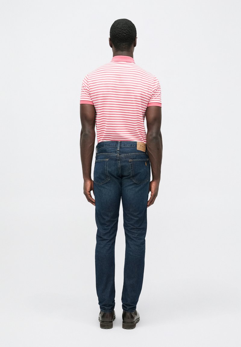 Red and white striped polo shirt, snug fit, paired with dark blue jeans, straight leg design, and brown boots, viewed from behind.