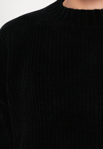 Black corduroy sweater with a textured, ribbed design and a high neckline. The fabric appears soft and plush.