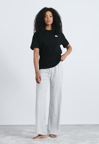 Crna majica kratkih rukava s suptilnim logotipom, uparena sa svjetlosivim širokim hlačama, stvara ležeran outfit.