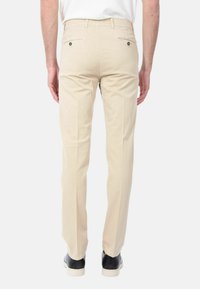 Chino beige con una vestibilità slim, dotati di due tasche posteriori con bottoni e una texture liscia. I pantaloni sono abbinati a sneakers nere.