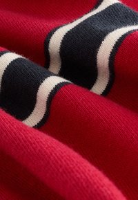 Suéter de punto en rojo, con patrones de rayas onduladas en negro y crema. Textura suave, con una vista en primer plano que resalta la estructura tejida del tejido.