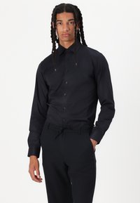 Black long-sleeve shirt in a smooth, matte fabric with a button front, classic collar, and fitted design, paired with black pants.