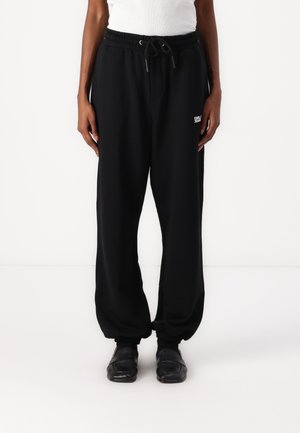 Black sweatpants with elastic waistband and drawstring. Cuffed ankles and small white logo detail on upper left leg. Soft fabric texture.
