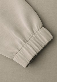 Manchette en tissu beige avec poignet élastiqué, présentant une texture côtelée fine et un détail de couture sur un fond de matériau lisse.