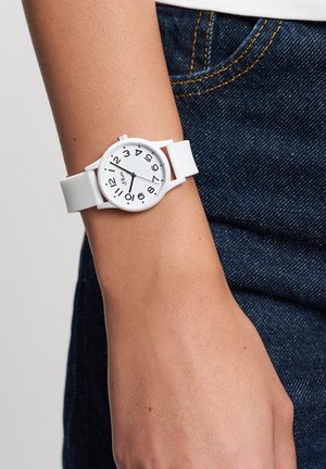 White silicone wristwatch with large black numbers on a round face; smooth texture, minimalist design, secured with a matching band.