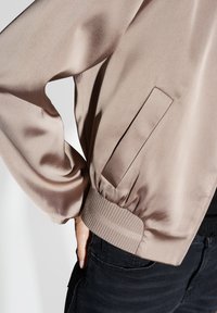 Lichtbeige bomberjack van gladde stof, met een ribgebreide zoom, elastische manchetten en een discreet zijzakje.