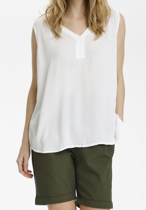 Blouse blanche sans manches avec col en V et détail de poche, en tissu texturé. Associée à un short vert olive retroussé.