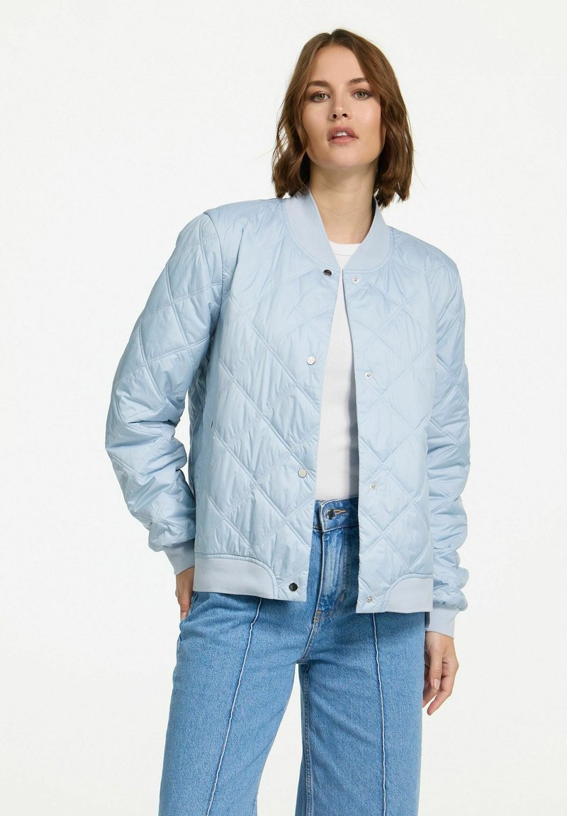 Lichtblauwe gewatteerde bomberjack met drukknoopsluitingen, geribde manchetten en een gladde textuur. Gestyled met een wit topje en hoge taille jeans.
