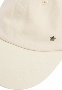 Cappello beige chiaro in tessuto a coste con visiera curva e accento metallico a forma di stella sui lati. Presenta dettagli di cucitura a vista.