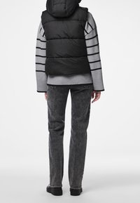 Svart pufferväst över en grårandig tröja, parat med grå avsmalnande jeans och svarta skor. Texturerat tyg med synliga sömmar.