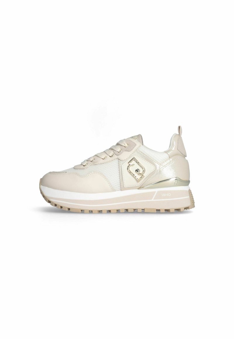 Beige Sport Schuh mit einem strukturierten Mesh- und glatten Leder-Obermaterial, ausgestattet mit einem metallischen Akzent und einer dicken, gemusterten Gummisohle.
