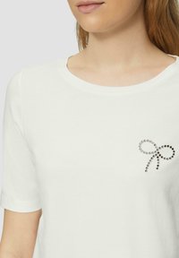 Witte katoenen T-shirt met een ronde halslijn en korte mouwen, met een strikmotief bezaaid met kristallen op de linkerborst.