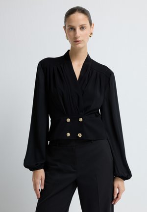 Mustalmeidät, joissa on laskostetut olkapäät, pitkät puffihihat ja istuva vyötärö. Koristeena kultasävyiset kaksoispainikkeet. Sujuva kangas.