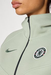 Világoszöld Nike zipzáros dzseki magas gallérral, a Chelsea Football Club logójával és sötétzöld swoosh részlettel.