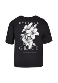 Sort t-shirt med korte ærmer, der har et hvidt blomstermotiv med liljer og en sommerfugl samt teksten "ETERNAL GRACE" foran.