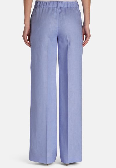 Lichtblauwe wijde broek met elastische tailleband, gedragen door een persoon die van achteren wordt getoond tegen een effen achtergrond.