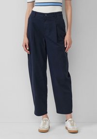 Pantaloni a gamba larga blu navy con pieghe frontali, realizzati in cotone, con chiusura a bottone e tasche laterali, abbinati a sneakers bianche.