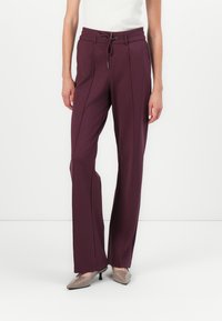 Pantalon ajusté bordeaux avec taille haute, cordon de serrage et coutures verticales pour un look épuré. Tissu lisse, forme des jambes évasées et éclat subtil.