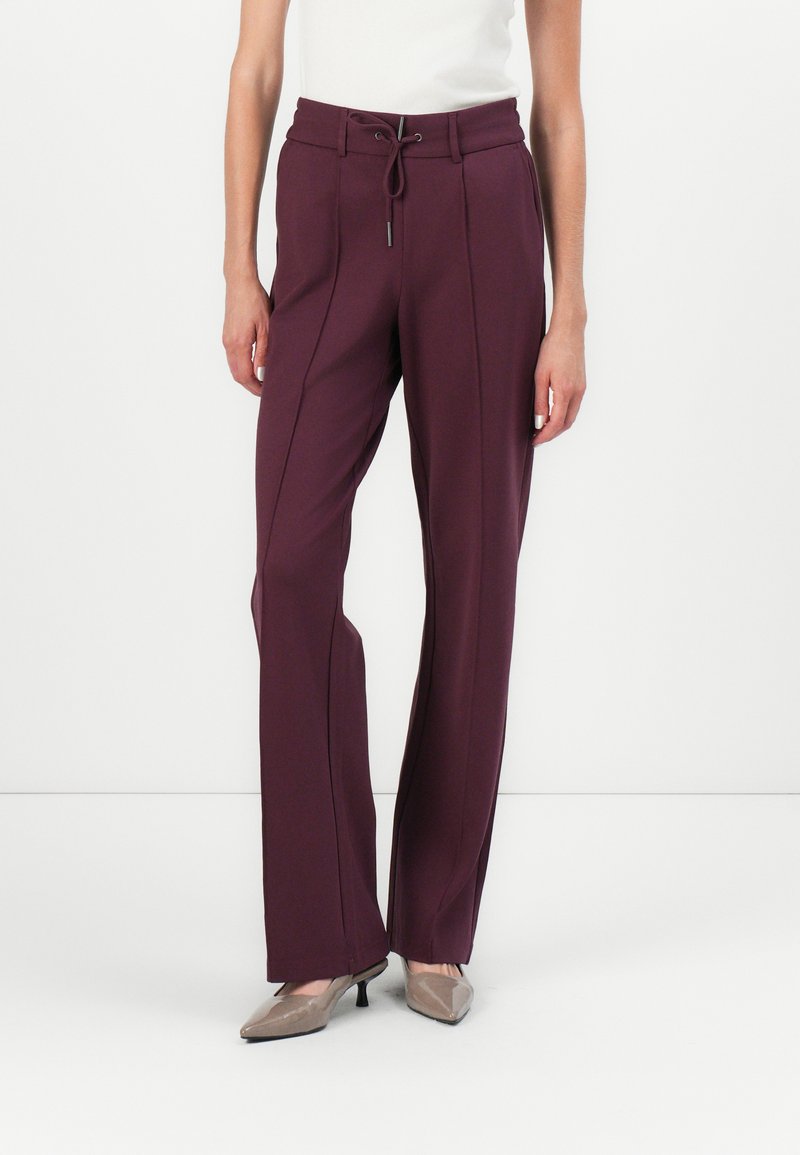 Pantalon ajusté bordeaux avec taille haute, cordon de serrage et coutures verticales pour un look épuré. Tissu lisse, forme des jambes évasées et éclat subtil.