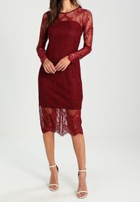 Burgundy lace dress with long sheer sleeves, intricate floral patterns, and a scalloped hem, paired with beige ankle strap heels.