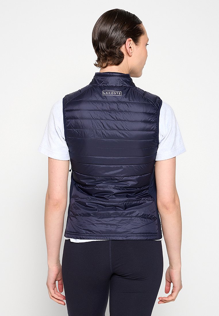 Gilet rembourré marine avec un col haut, design matelassé horizontal et une étiquette de logo à l'arrière. Matériau en nylon léger avec une texture lisse.