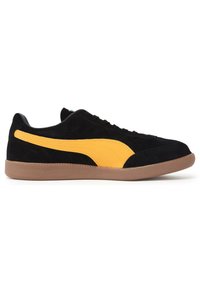 Zapatillas de ante negro con una franja amarilla de PUMA, que cuentan con una suela de goma texturizada y cordones negros. Diseño de perfil bajo.