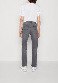 Grå denimjeans med rak bendesign, bakfickor med stickade accenter, bärs med en vit t-shirt och ljusa sneakers.