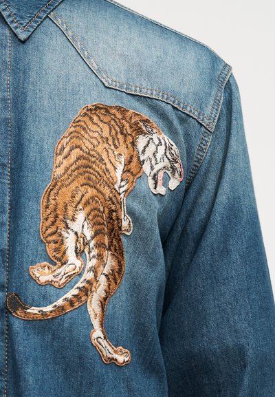 Τζιν μπουφάν με λεπτομερές κεντητό έμβλημα ενός λιονταριού που ουρλιάζει στο πάνω μέρος της πλάτης κοντά στη ραφή του ώμου.