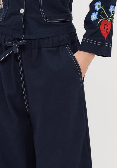 Tums zilas kokvilnas drēbes ar baltu šuvumu, atvieglota josta ar auklu un ziedu izšuvums uz piedurknes, attēlojot sirdi.