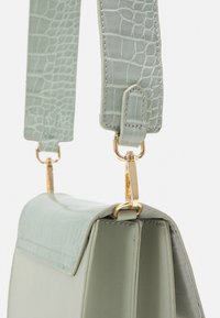 Zelená kabelka v mátové barvě s texturovaným krokodýlím vzorem. Obsahuje zlacené kovové doplňky a má strukturovaný tvar s plochým vrchním klopou a nastavovacími popruhy.