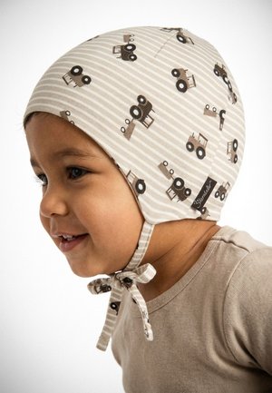 Toddler wearing beige striped bonnet with brown tractor prints, smiling and looking to the left, tied under the chin with a bow.