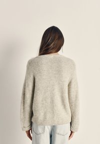 Hele halli, pehmea ja kohev kudum, ümmarguse kaelusega ja ribakujulise äärisega. Omab langetatud õlgu ja pikki varrukaid. Kantud helesiniste teksadega.