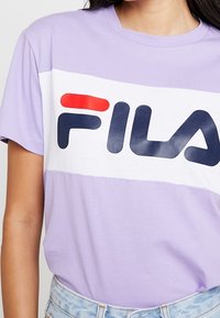 Lavender cotton t-shirt with a white horizontal band featuring a red and navy logo "FILA," short sleeves, and a relaxed fit.