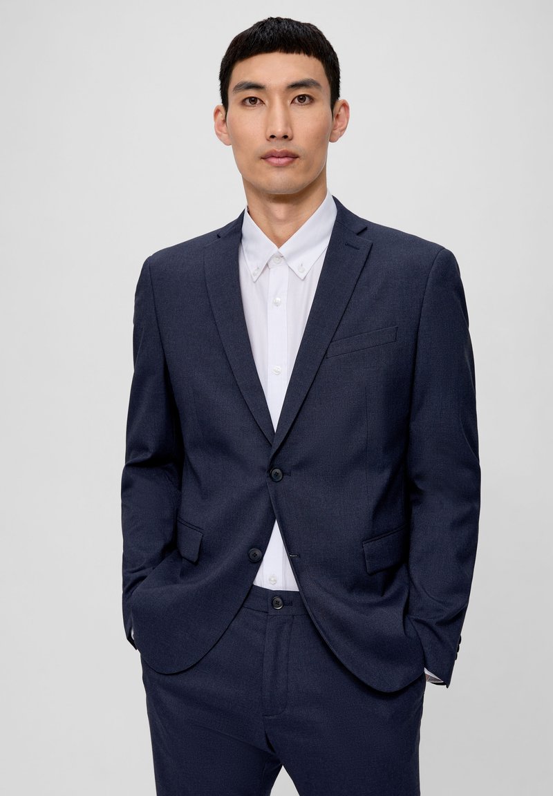 Marineblauer Anzug mit glatter Textur, einreihiger Jacke, Reverskragen und passender Hose über einem weißen Hemd mit Kragen.