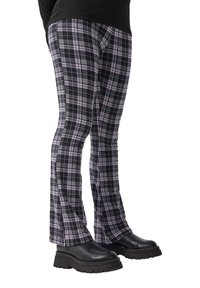 Czarno-fioletowe spodnie w kratę o rozszerzanym kroju, dopasowane do sylwetki, w połączeniu z masywnymi czarnymi butami na platformie. Gładka tekstura, widoczny wzór w kratę.