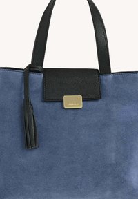 Sac en toile bleu en suède avec poignées en cuir noir, rabat en cuir noir, accent en pampille et fermoir rectangulaire doré sur un fond uni.