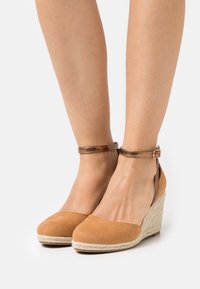 Décolleté con zeppa in suede beige, dotate di cinturino alla caviglia, dettagli in juta texture sulla zeppa e punta arrotondata.