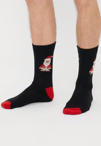 Fekete zoknik piros orral és sarkal, Mikulás mintázattal. Az anyag simának tűnik, kötött textúrával.