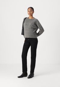 Szürke, bordázott pulóver széles ujjal, fekete, slim-fit farmernadrággal párosítva. A modell fekete bokacsizmát visel, és egy kis fekete táskát hord.